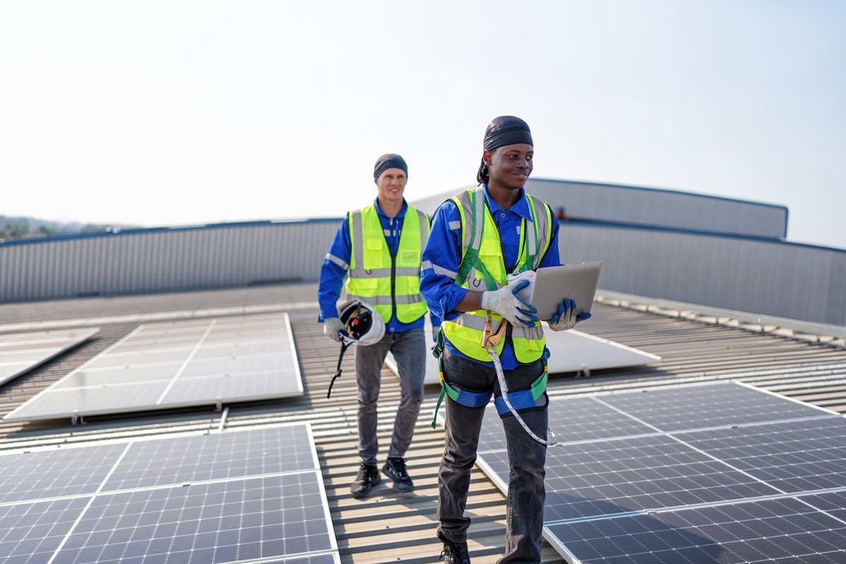 Engineer on rooftop stand next to solar panels discussion with team check laptop for solar installation